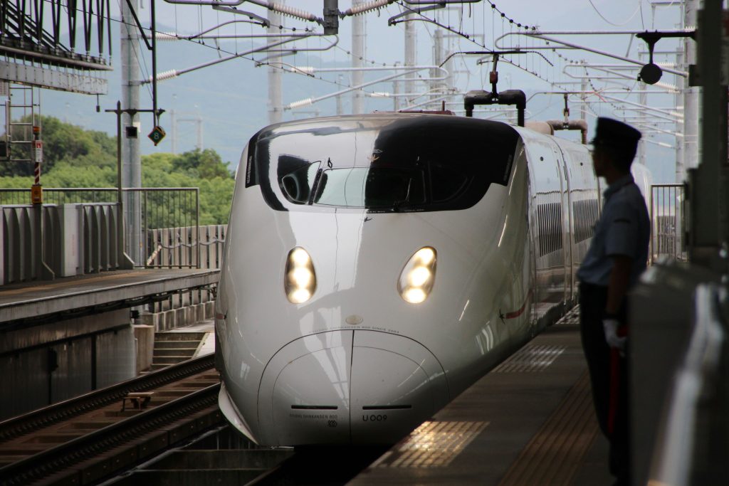 Ultra-modern white electric train locomotive with headlights on at modern train platform, and the silhouette of a man wearing train conductor uniform standing on the platform beside the train. Credit: Rikku Sama on Unsplash